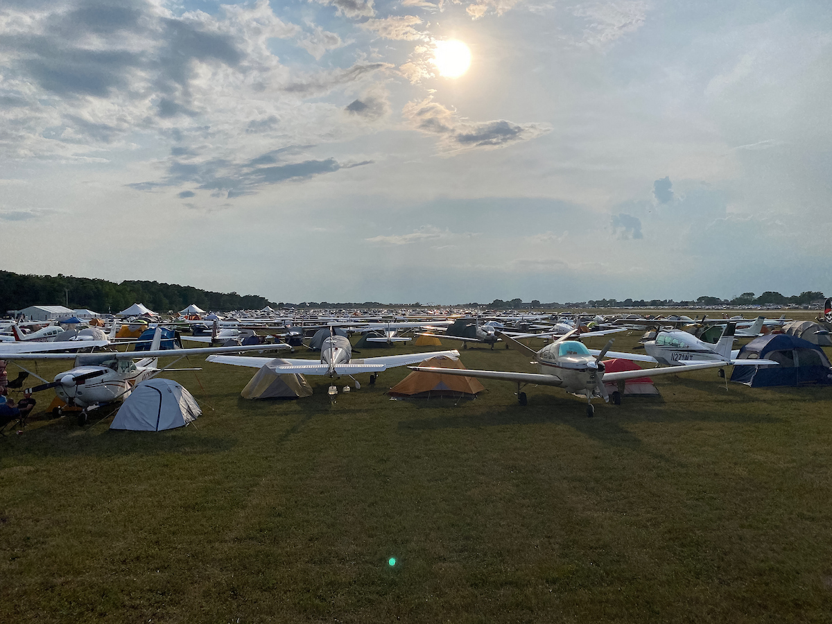 Large fly-in with airplanes and tents parked across a grass field